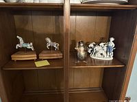 Porcelain figurine of a boy with two goats and a metallic penguin figurine on a cabinet shelf.