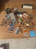 Overview of all items laid on wood floor showing playing cards, marbles, pins, small trinkets, and tools in a box and scattered around