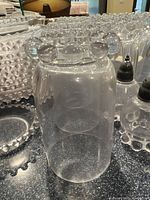 Close-up image of a cylindrical glass container with distinctive beaded pattern on the rim, salt and pepper shakers visible in the background.