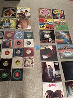 Wide view of vinyl records laid out on carpet showing album covers and singles.