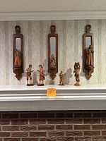 Wide view of mantel showing three wall-mounted mirror hangers each with attached figurine, and four freestanding figurines on shelf below.