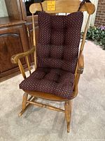 Front view of vintage wooden rocking chair with tufted burgundy cushion showing condition and design.
