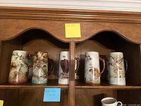Front view of five ceramic wildlife steins on wooden shelf showing designs and handles