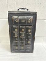 Front view of one wine bottle carrier showing faux book spines with titles Treasure Island, Notre Dame De Paris, and Emma 1899 in gold embossing on black material.