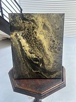 Front view of abstract painting showing swirling black, gold, and beige patterns on canvas.