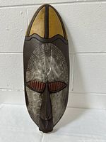 Front view of the elongated oval African wall mask showing the wooden frame and embossed metal insert with detailed patterns.