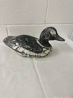 Side view of the black and white painted wooden duck decoy showing its carved body and paint wear.