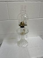 Full view of the entire glass oil/kerosene lamp showing the clear glass base, fuel reservoir, metal burner, and chimney