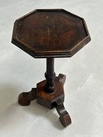 Photo of antique octagonal wooden table with turned central column and three curved legs on concrete floor.