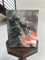 Front view of the small abstract acrylic painting on canvas with fluid pouring technique and vibrant colors including black, white, red and turquoise.