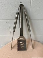 Photo showing pair of BBQ tongs and slotted spatula held together showing handles with hanging loop