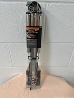 Front view of the 9-piece BBQ tool set with all tools hanging on clear acrylic stand against white wall.