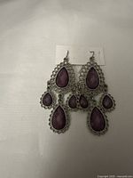 Front view of the pair of silver-tone 3-tier dangle earrings with purple faceted teardrop stones on a white background.
