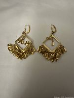 Pair of gold color tassel earrings laying side by side on a light fabric background, showing front and back views.