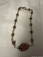 Full view of the necklace showing the orange and black swirl round beads and large oval pendant centerpiece with metal chain links and clasp.