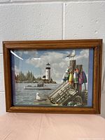 Full frontal view of wooden picture frame showing lighthouse and seagulls scene, set against white wall.