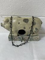 Front view of pig-shaped bird house showing entrance hole, painted details and attached chain.