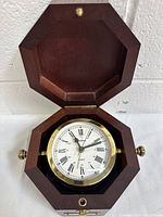 Open wooden octagonal box showing the vintage Bulova quartz clock inside, brass bezel and white dial with Roman numerals