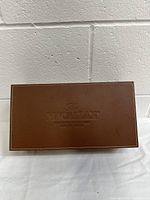 Closed rectangular brown leather whiskey case embossed with Macallan logo on top