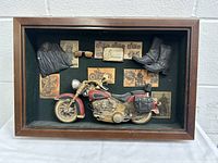 Full view of the shadow box with motorcycle, mini jacket, boots, and surrounding prints.