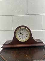 Full view of the dark brown wooden mantel clock case showing the overall shape and finish. The clock face is visible with Roman numerals and black hands.