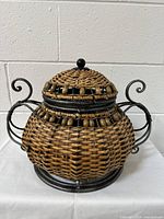 Front view of decorative wicker basket with metal frame, lid, knob, and handles.
