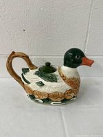 Side view of the duck-shaped porcelain teapot showing detailed painted feathers, handle, and lid.