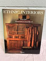 Front cover of Ethnic Interiors hardcover book shows wooden furniture with textured wood cabinet and orange garment, indicative of ethnic interior design themes.