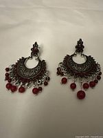 Front view of the ethnic style earrings showing intricate engraved silver metal and red rhinestone and bead details.