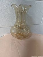 Full view of the beige vintage glass lampshade with ruffled edge sitting on a pink cloth surface against a white wall.