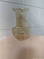 Side view of vintage beige glass lampshade with ruffled edge, showing narrow neck and bulbous bottom with polka-dot-like raised dots.