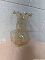 Front view of beige vintage glass lampshade with rounded bottom and ruffled neck edge, placed on a light beige surface against a white brick wall.