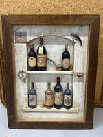 Full view of framed 3D shadow box showing miniature wine bottles, corks, and wine accessories on textured background.