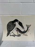 Print artwork showing a black and white loon interacting with a fish, depicted in a traditional style with artist initials TYC.
