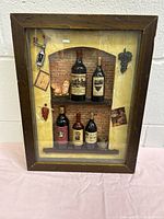 Front view of framed shadowbox art showing entire arrangement including miniature wine bottles, roosters, kitchen decor items, and paper decorations.