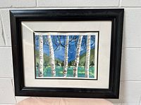 Full view of framed watercolor painting showing birch trees with background of lake and hills under blue sky.