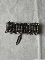 Top view of silver-toned hippie style wrist bracelet, showing textured vertical bars and attached feather charm.