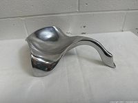 Angled side view showing the smooth and flowing form of the aluminum bird sculpture with reflective surface.