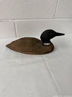 Side view of the wooden Canada duck decoy showing the brown wood-textured body, black head with red glass eye, and white neck markings.