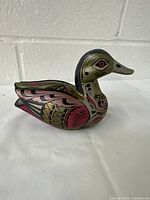 Side view of the hand-carved and painted wooden duck figurine showing intricate folk art style details in red, gold, and black.