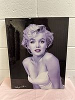 Front view of Marilyn Monroe black and white glossy print leaning against white brick wall.