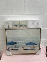 Front view of the boxed wall art set showing one canvas with blue umbrellas on the beach and promotional box insert with images of both pieces.