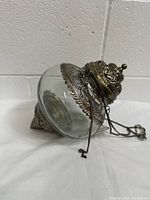 Side view of the glass pendant light-lamp lying on its side showcasing the clear glass body and intricate metal top with hanging chain.