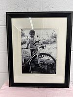 Front view of the black wooden photo frame with a vintage black and white photo of a child with a bicycle.