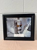 Framed photograph showing an urban scene detail with metal fixture and part of credit label visible.