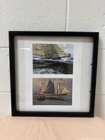 Front view of the black 12x12 inch picture frame hanging on a white textured wall. Shows the two nautical prints inside the frame.
