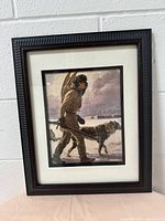 Full view of the framed print showing the winter scene with a man and dog, leaning against a wall.