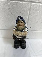 Front view of the pirate sailor figurine placed against a white brick wall, showing facial details and costume