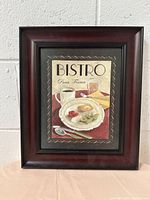 Full view of the framed poster titled 'BISTRO, Paris, France' showing the food and drink illustration in a dark wood frame against a light wall background.