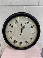 Full view of the large round quartz wall clock with black frame, Roman numerals, and decorative design on face.